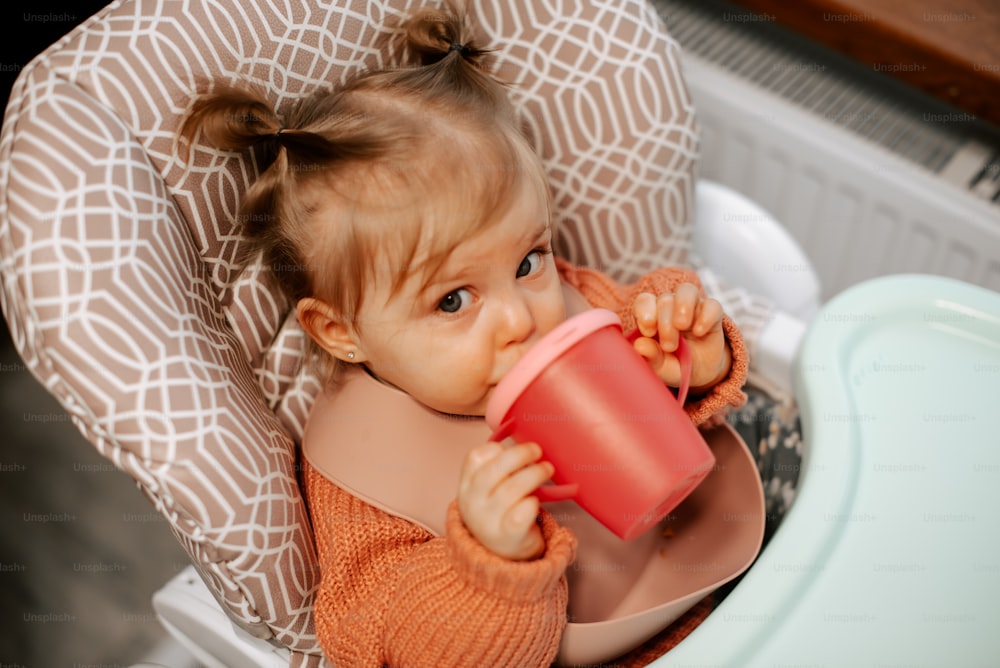 a little girl sitting in a high chair drinking out of a cup