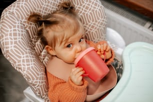 a little girl sitting in a high chair drinking out of a cup