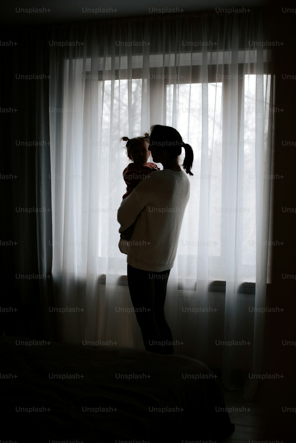 a woman holding a child in front of a window