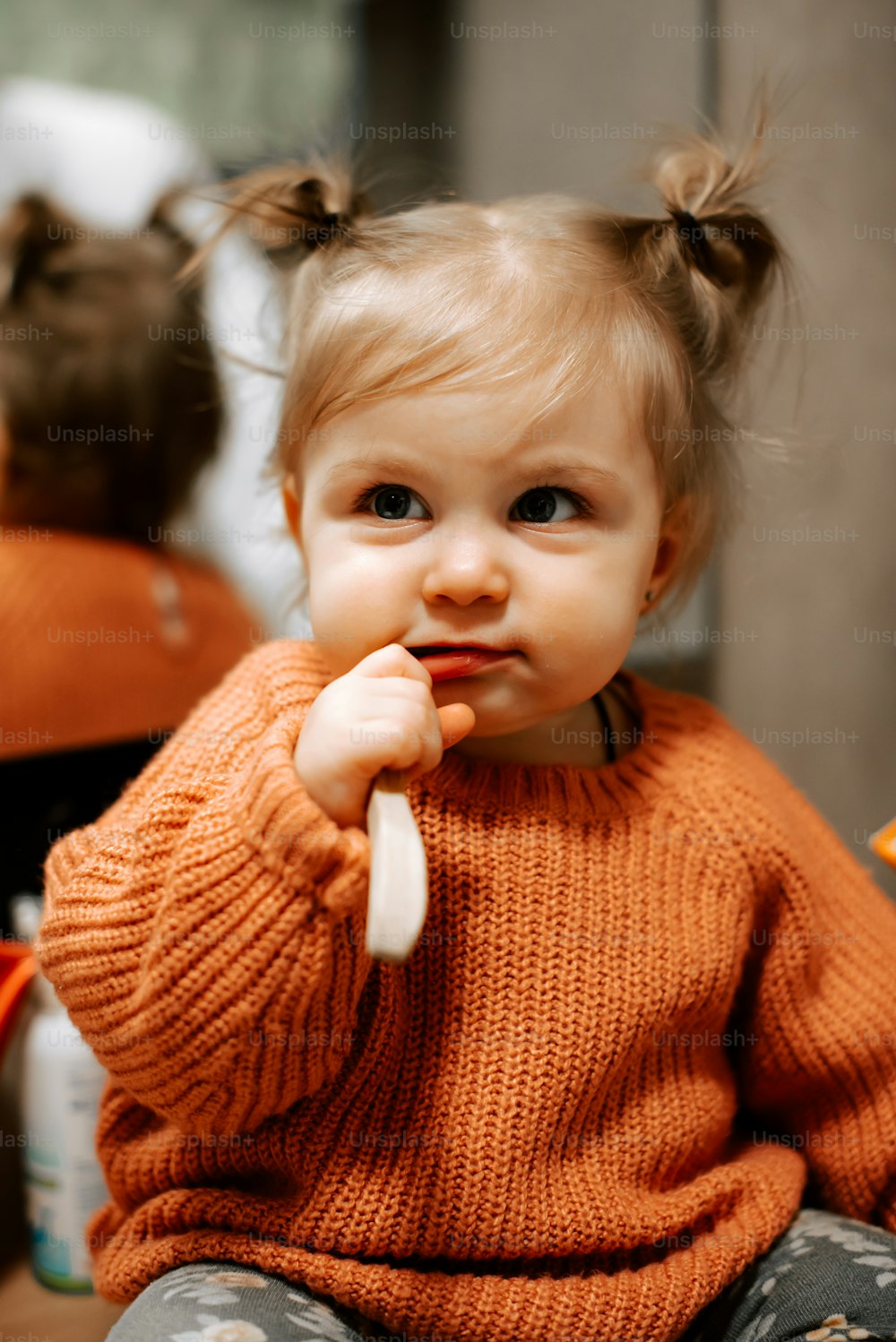 a little girl sitting on the floor with a toothbrush in her mouth