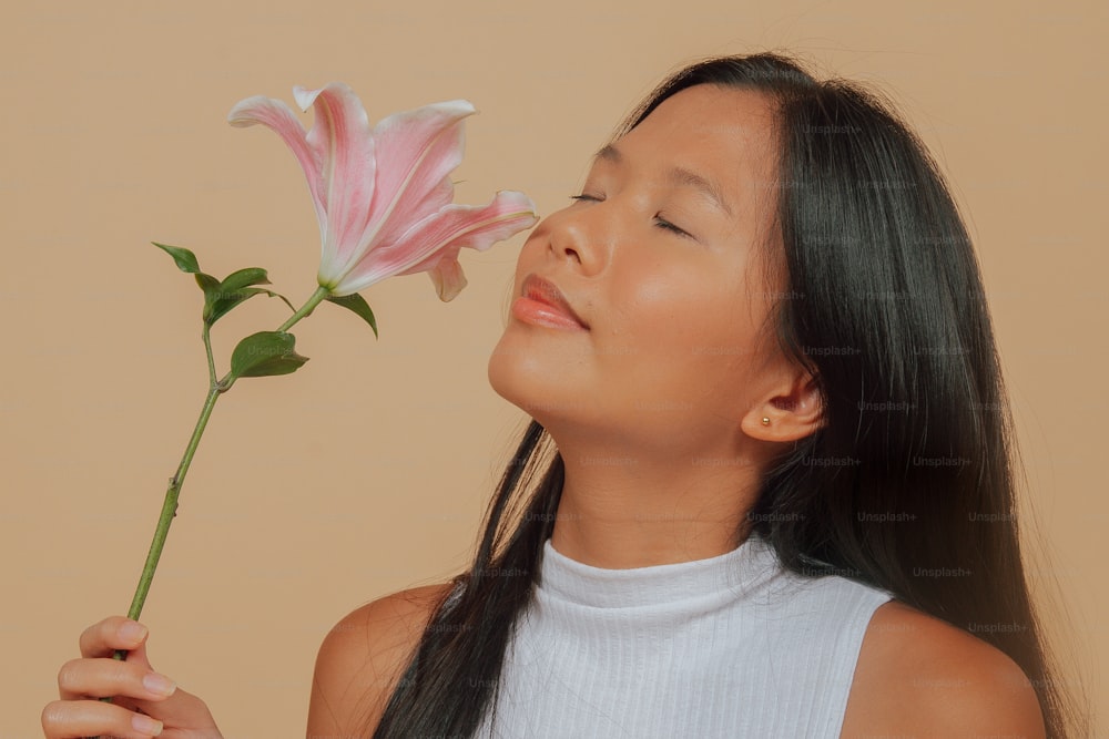 Ein junges Mädchen, das mit geschlossenen Augen an einer rosa Blume riecht