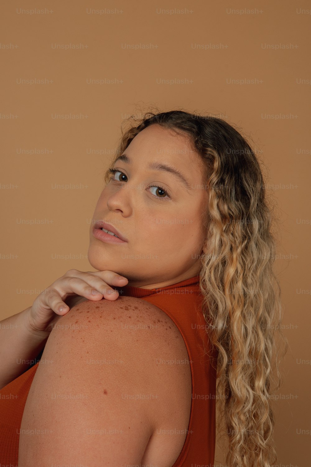 Eine Frau mit lockigem Haar trägt ein orangefarbenes Oberteil