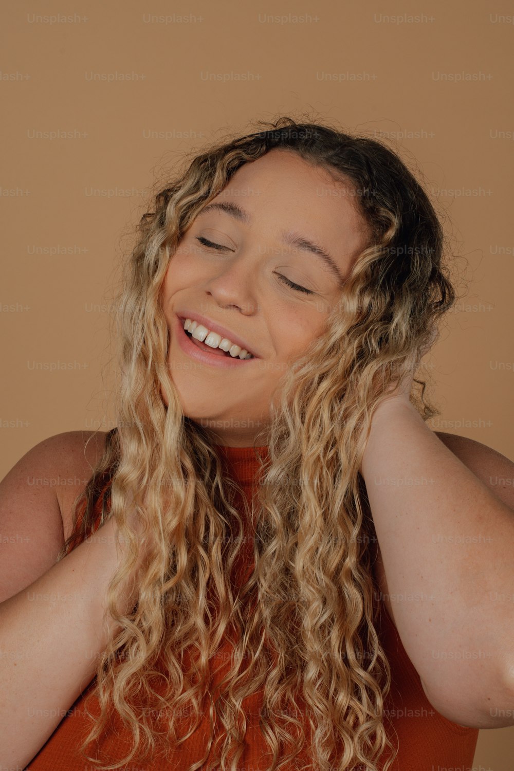 a woman with curly hair smiling and holding her hands behind her head
