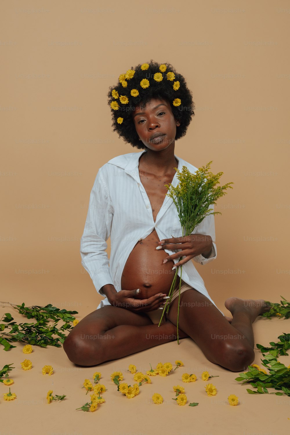 a pregnant woman sitting on the ground with flowers in her hair