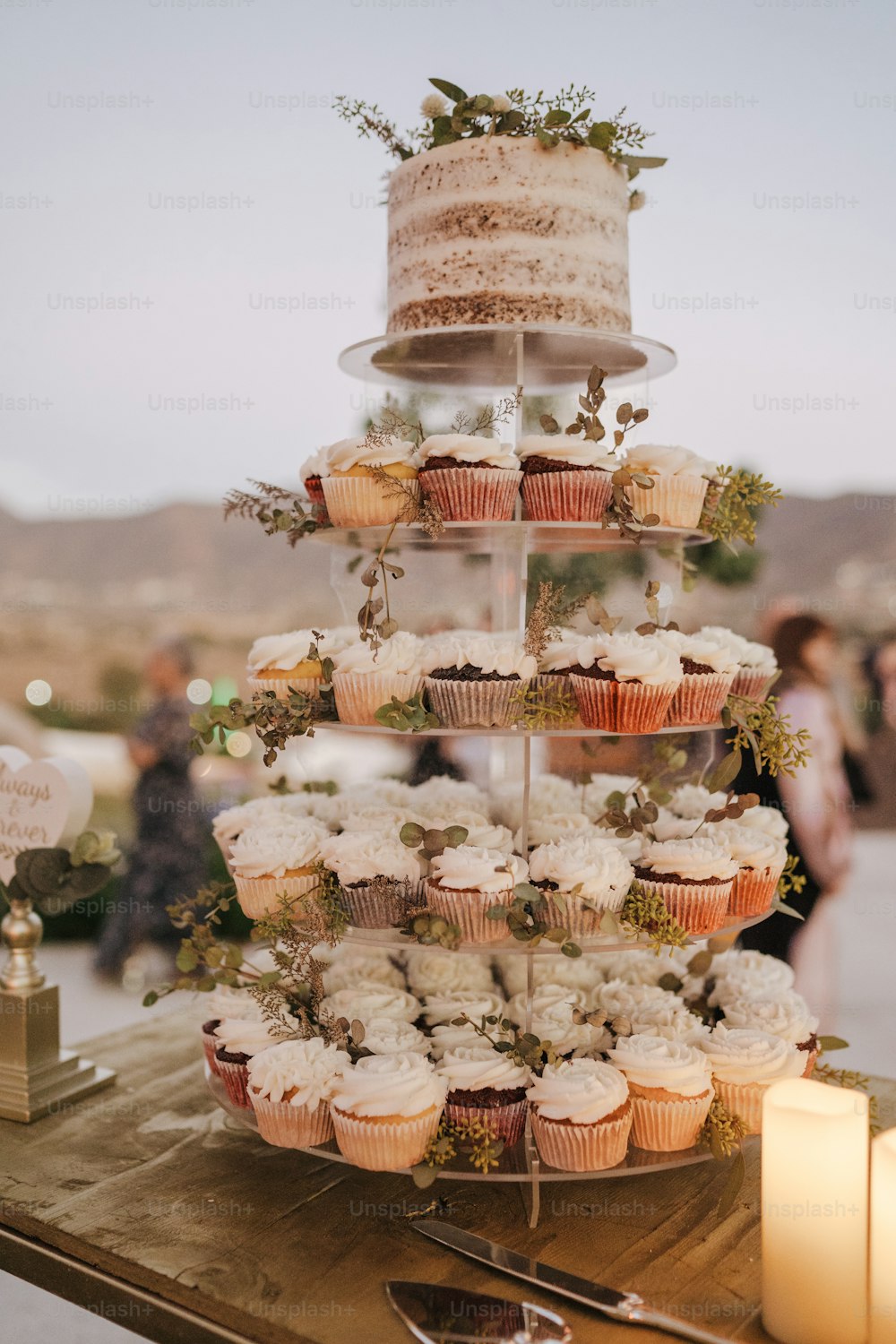 a tiered cake with cupcakes and greenery on it