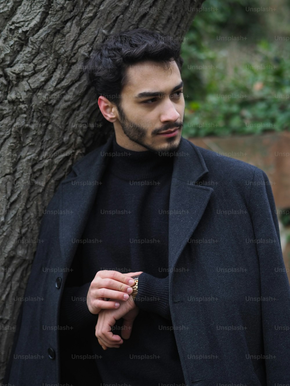 a man standing next to a tree wearing a black coat
