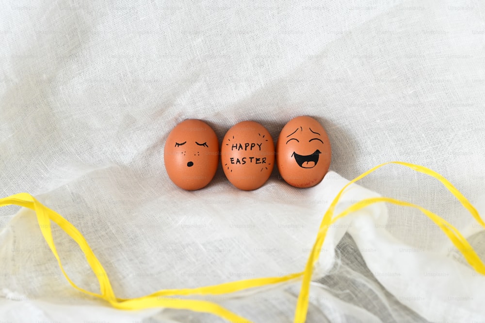 three eggs with faces drawn on them sitting next to a yellow ribbon