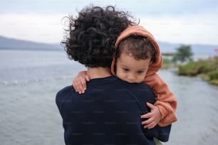 a woman holding a small child near the water