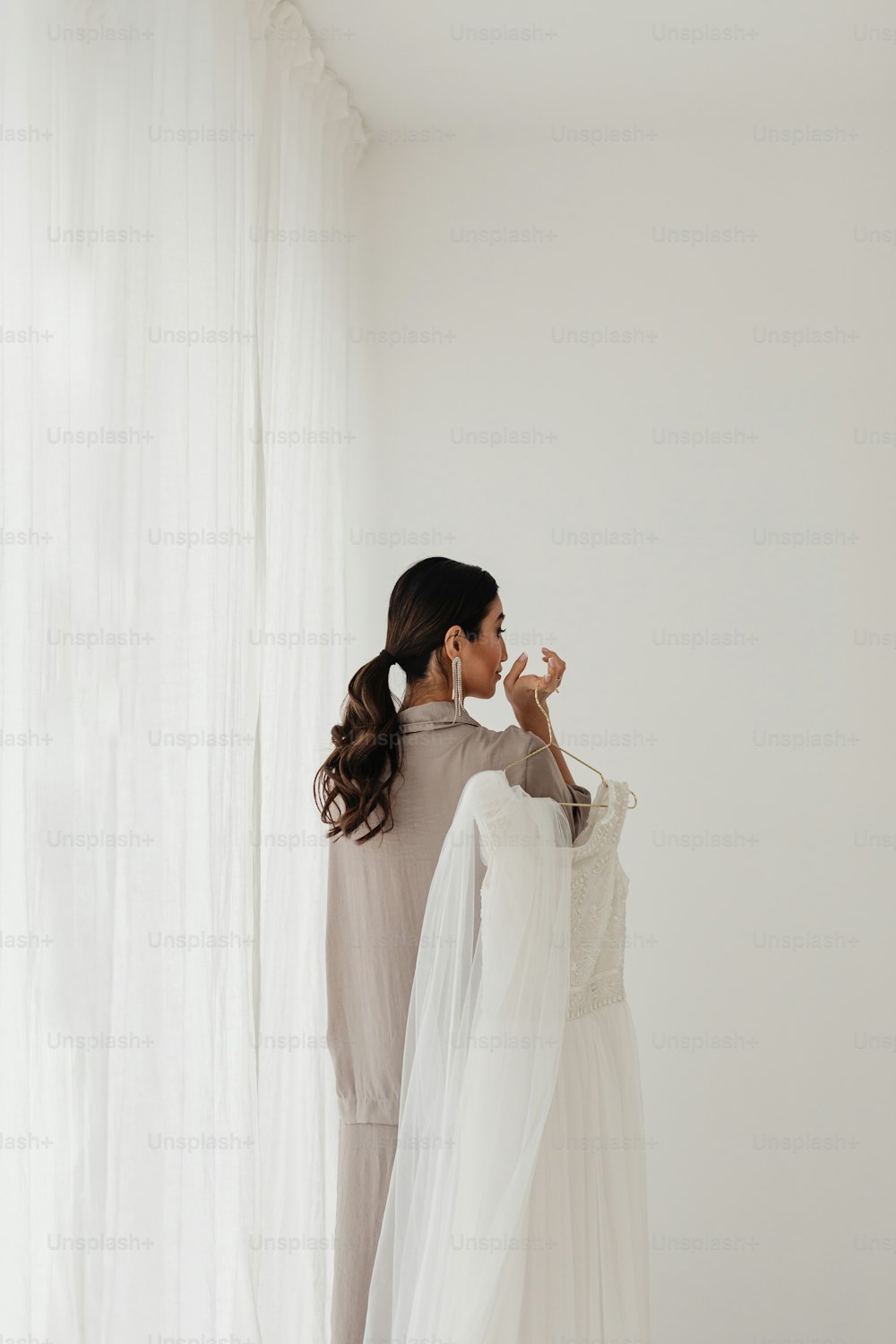 a woman standing in front of a white curtain holding a dress