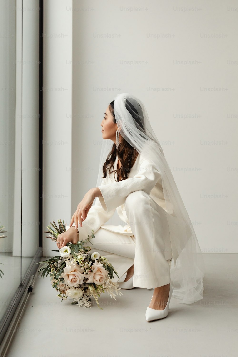 Una mujer con un vestido de novia arrodillada junto a una ventana