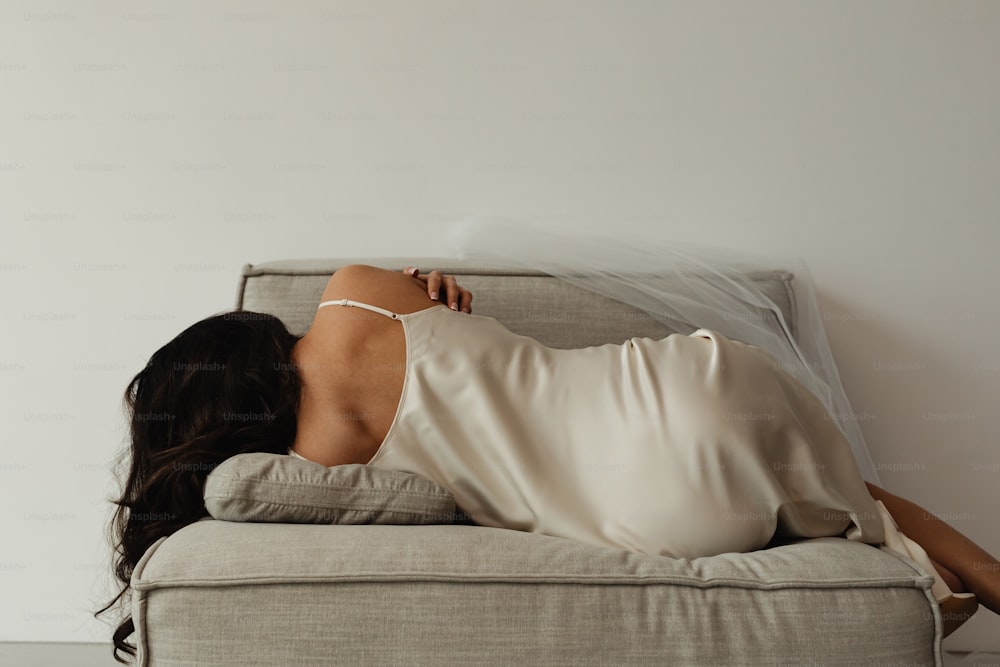 Une femme en robe blanche allongée sur un canapé