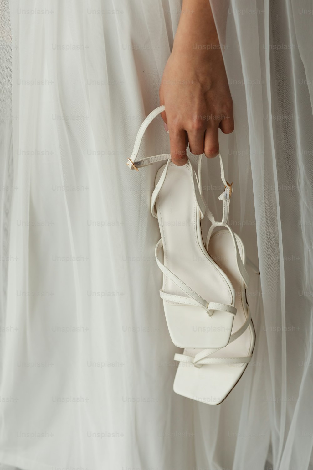 Eine Frau in einem weißen Kleid hält einen weißen Schuh