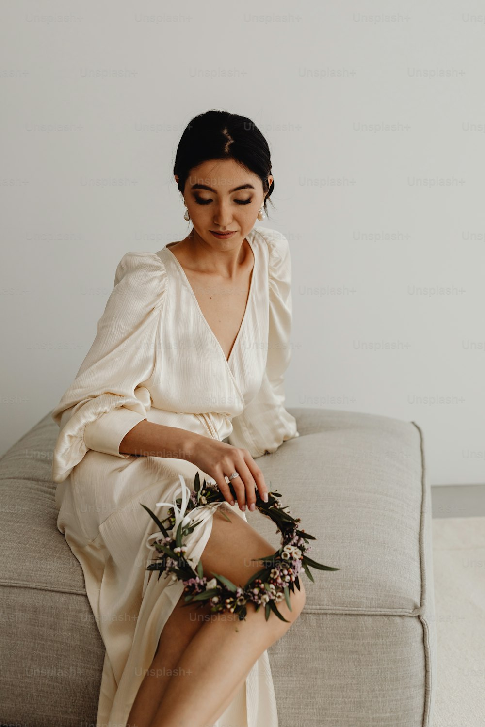 uma mulher sentada em um sofá com uma coroa de flores em torno de seus tornozelos
