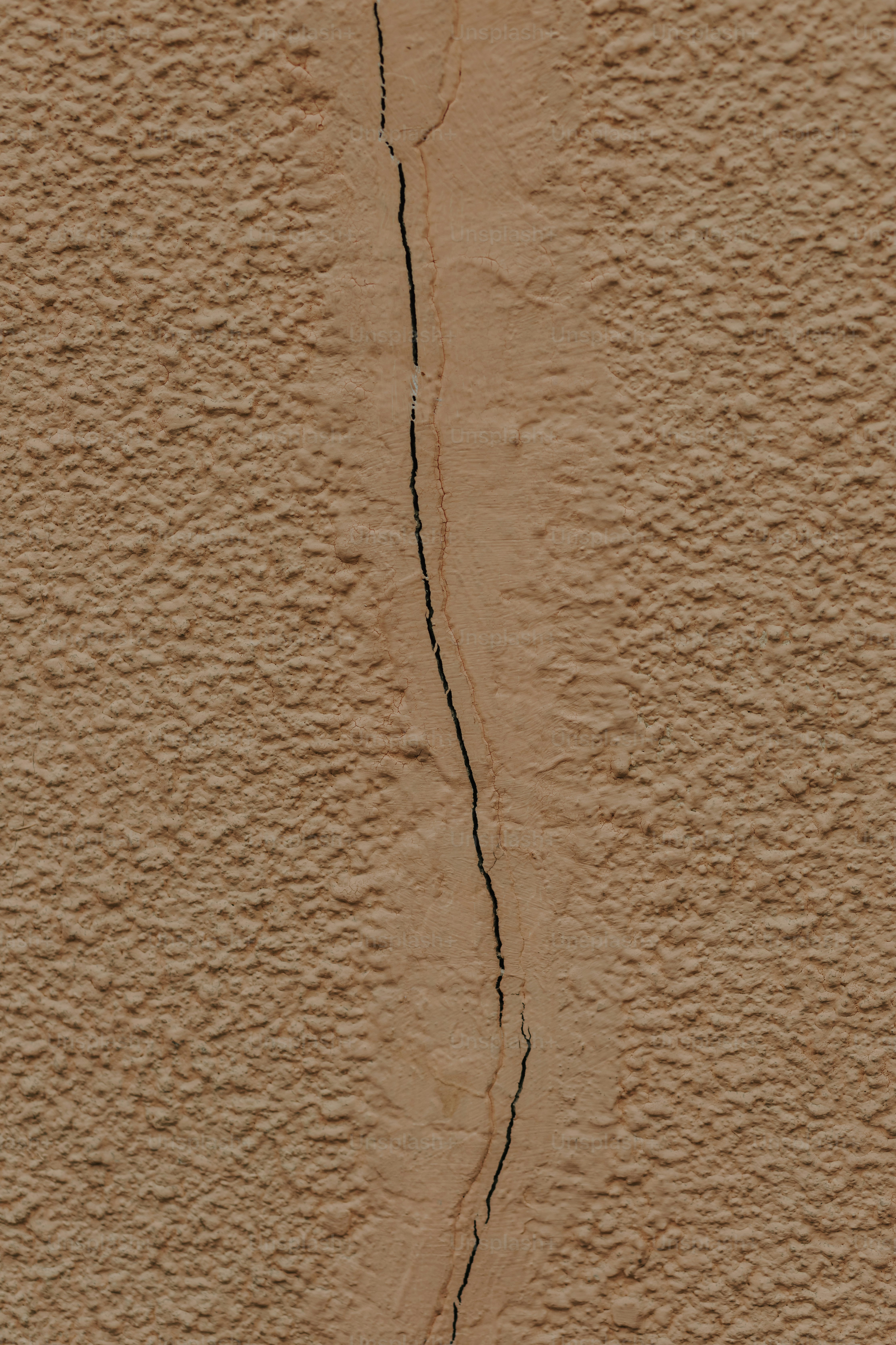 a red fire hydrant sitting in front of a crack in a wall