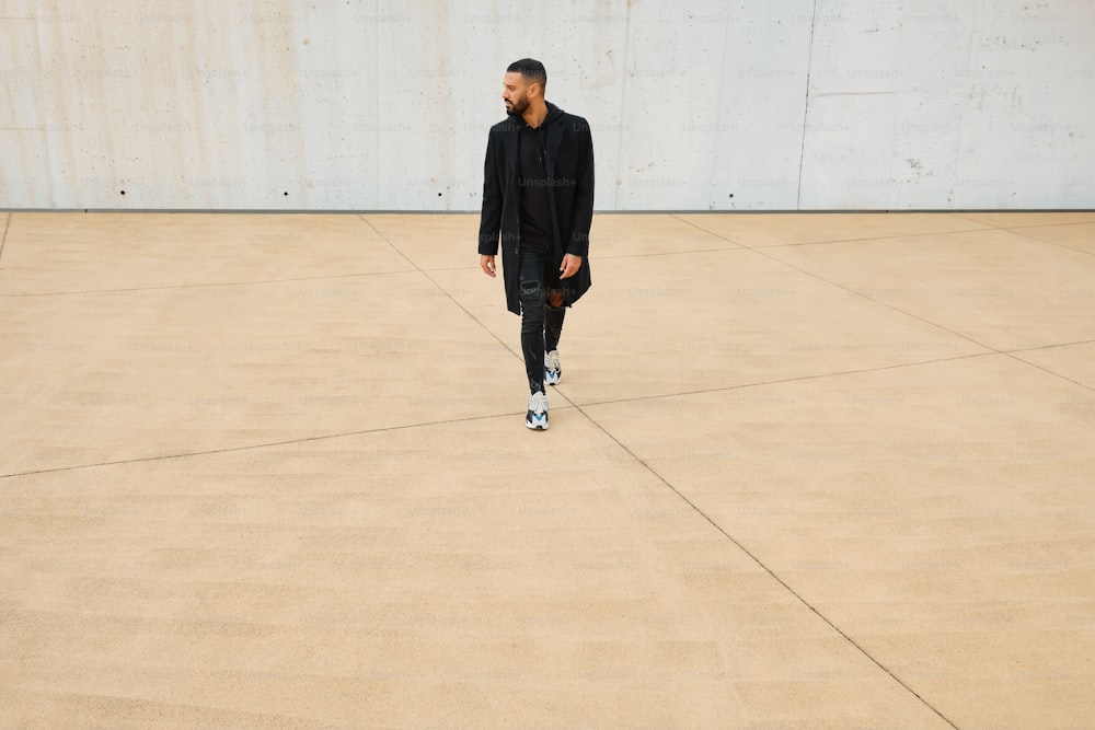 a man in a black suit walking across a cement floor