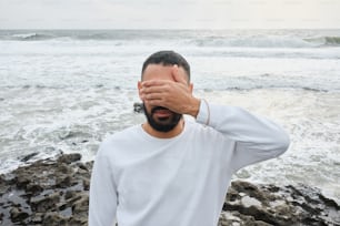Un hombre cubriéndose los ojos junto al océano