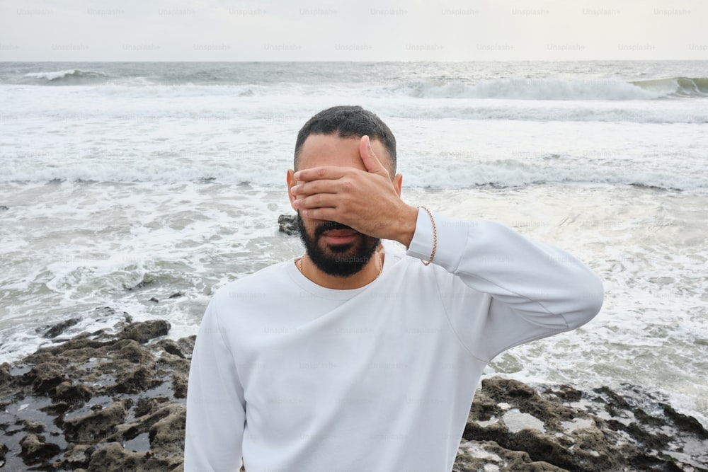 a man covering his eyes by the ocean