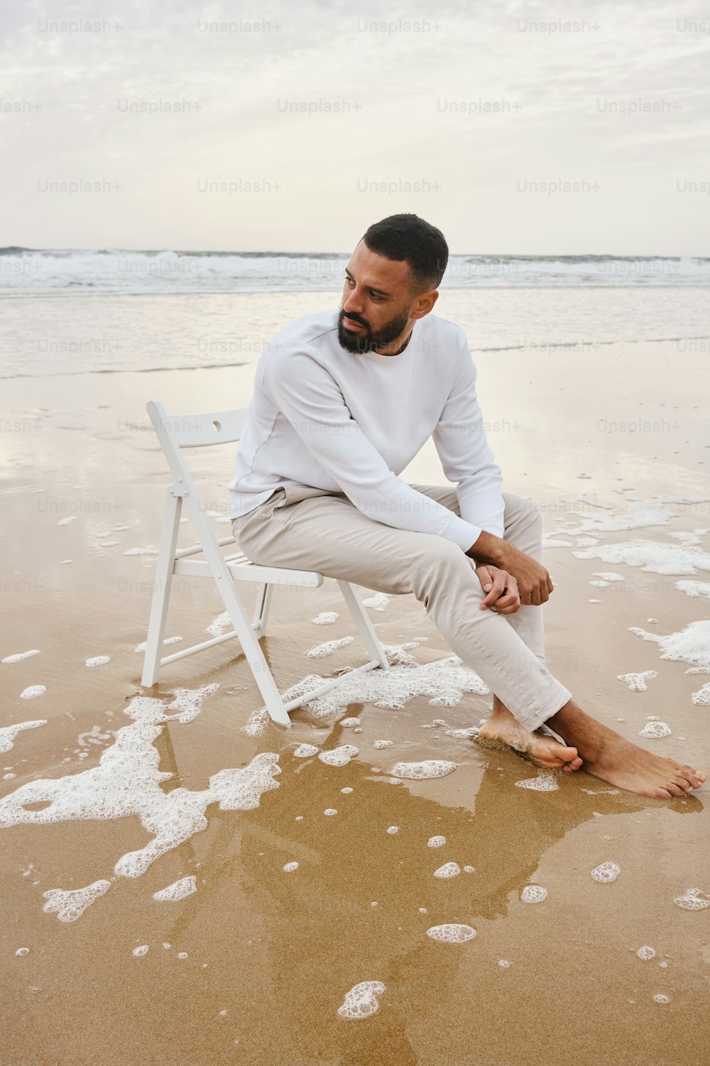 um homem sentado em cima de uma cadeira branca em cima de uma praia