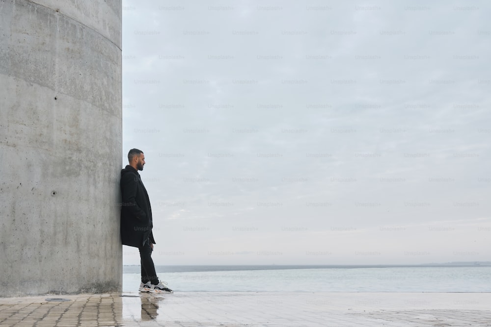 a man leaning against a wall near the ocean