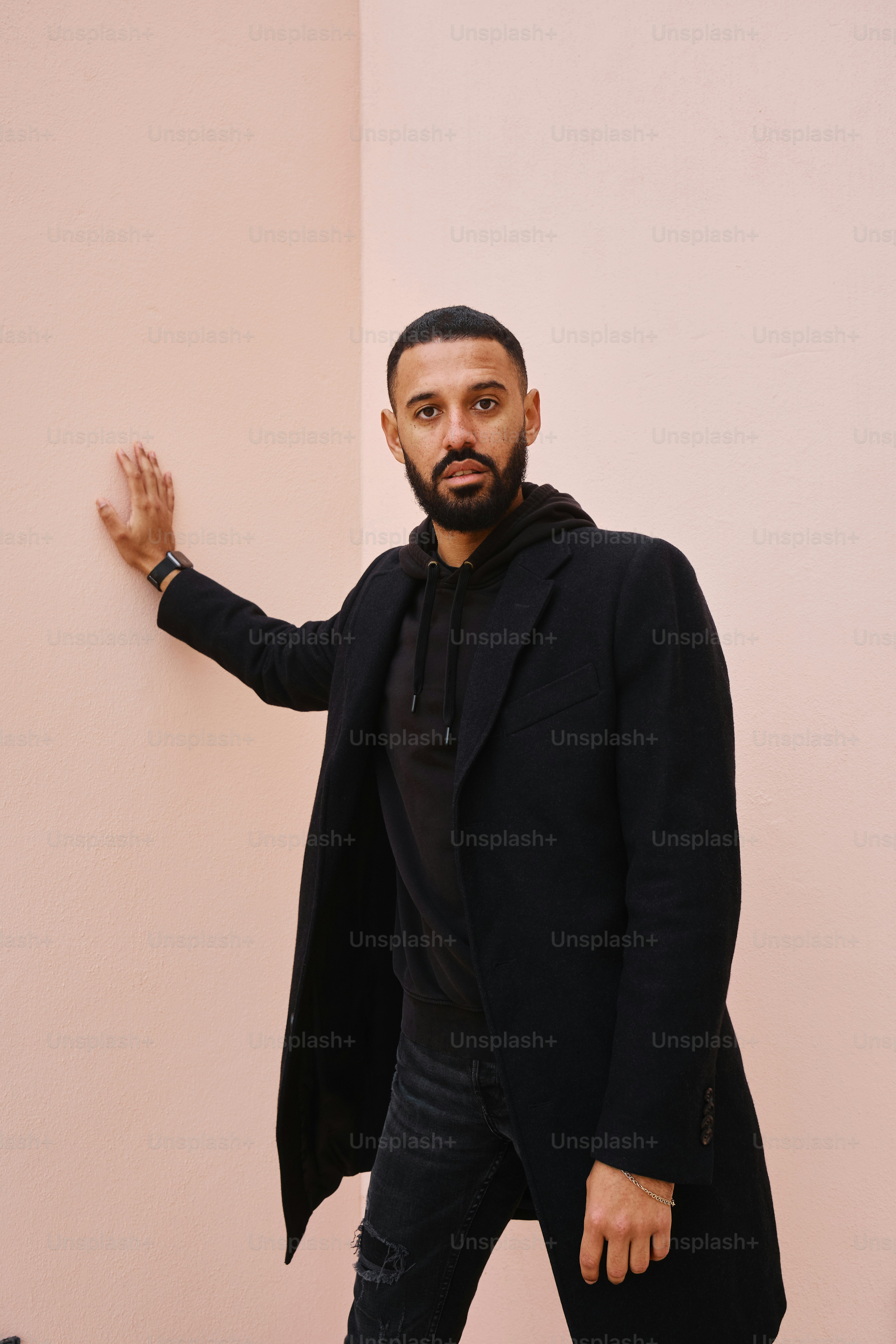 Un hombre con un abrigo negro apoyado contra una pared