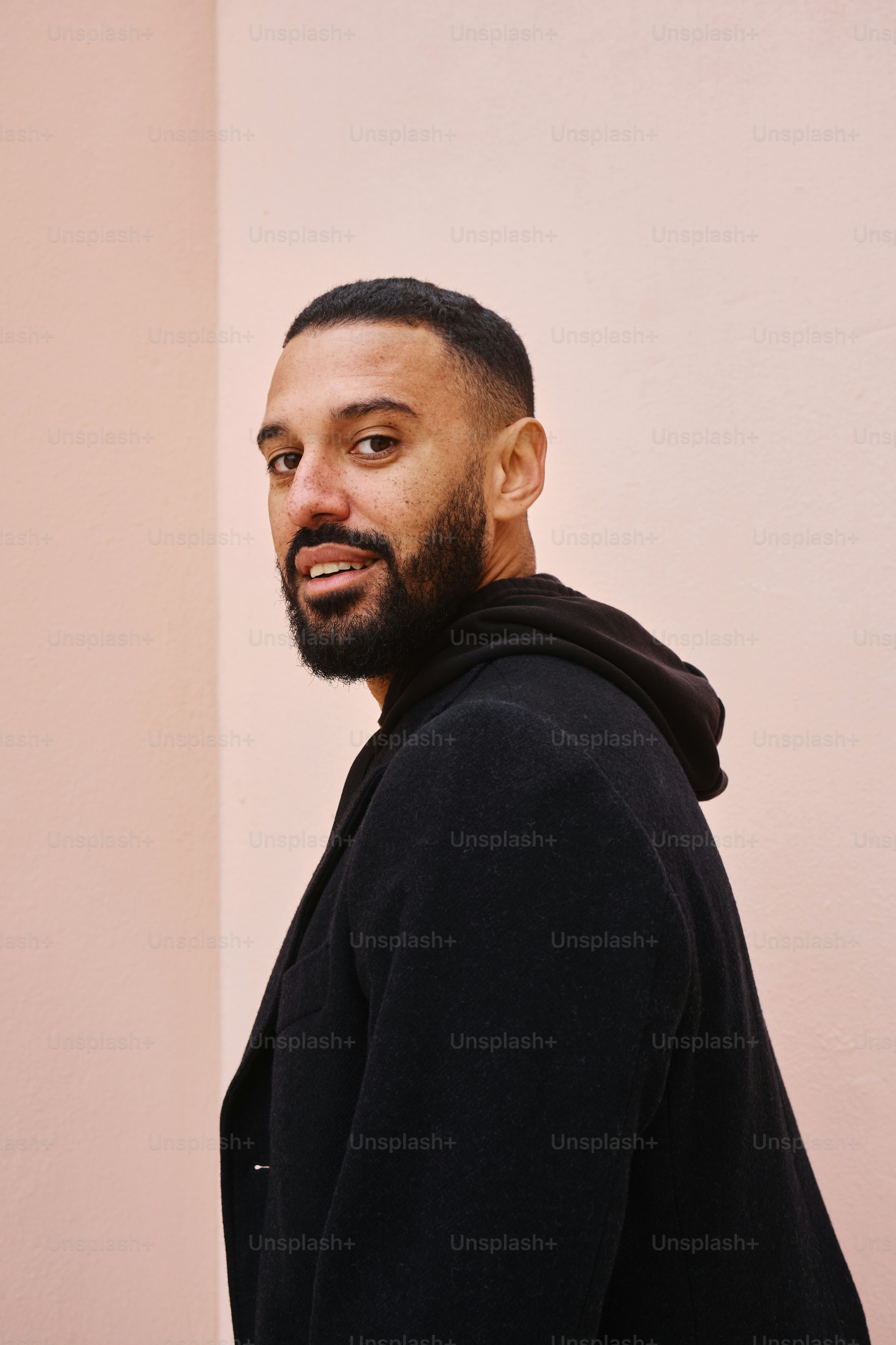 Fashion portrait of a handsome man in all black outfit look against a pink color background