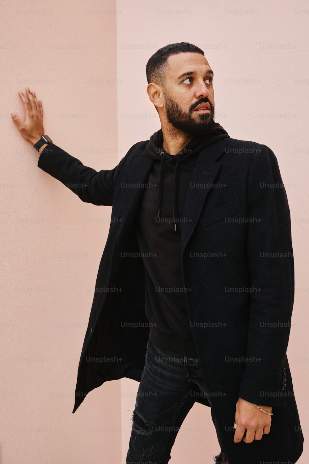 a man in a black coat leaning against a wall