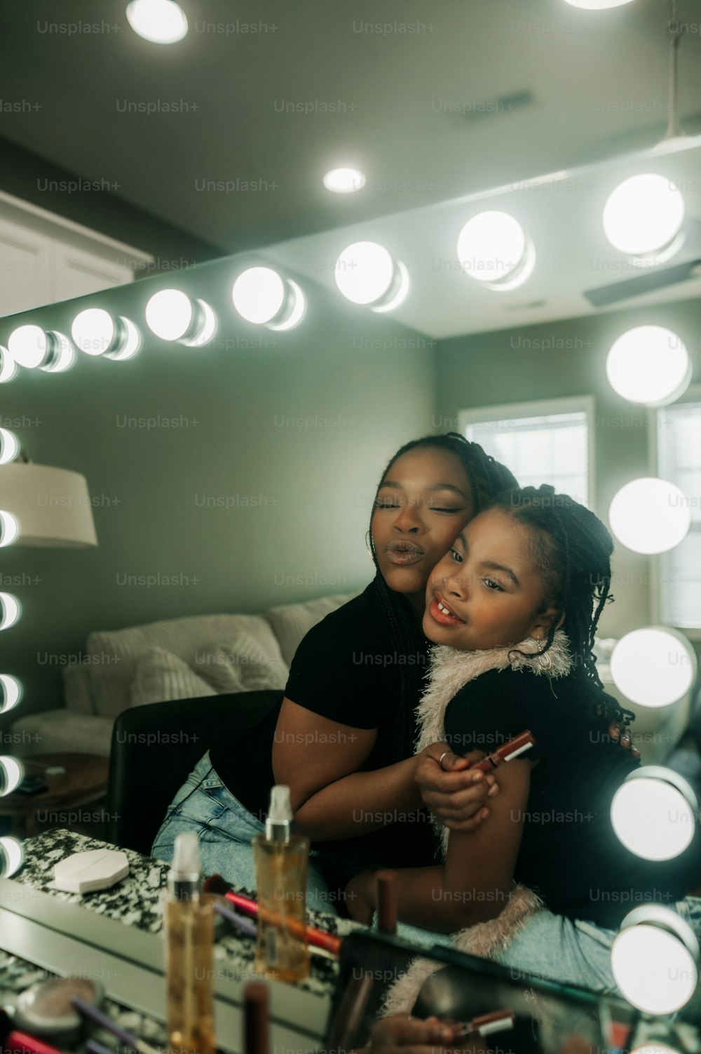 a woman sitting next to a little girl in front of a mirror
