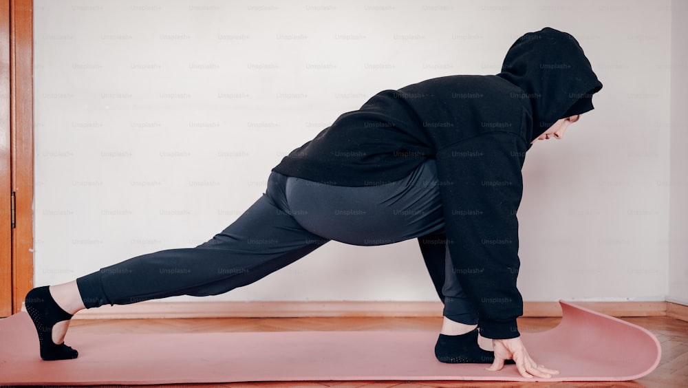 Eine Person in einem schwarzen Kapuzenpullover macht eine Yoga-Pose