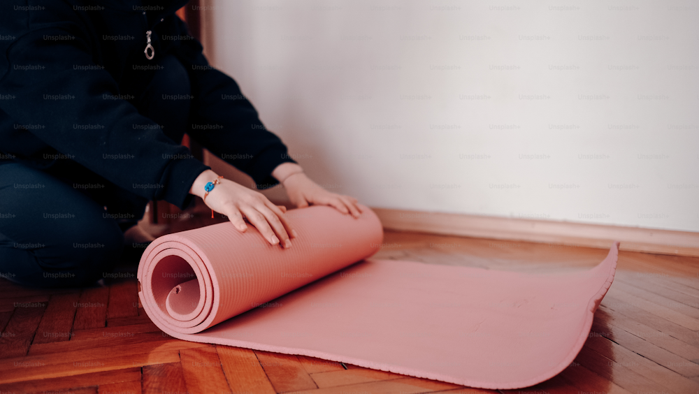 a woman is rolling up a pink mat on the floor