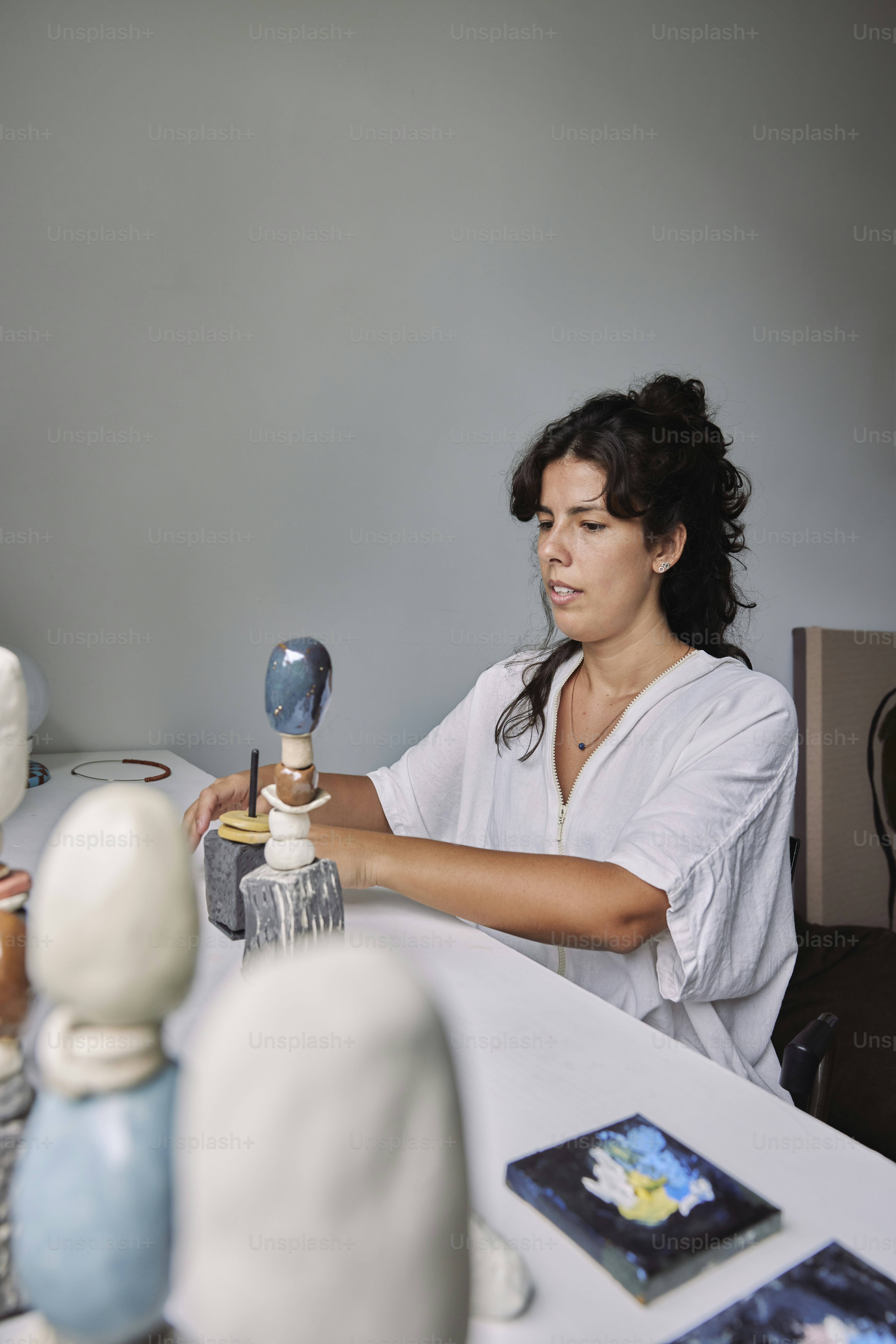 a woman sitting at a table working on a sculpture