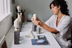 a woman sitting at a table working on a sculpture