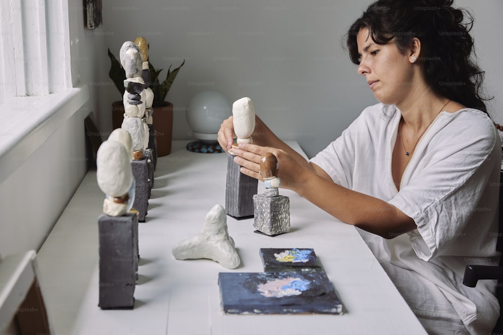 a woman sitting at a table working on a sculpture