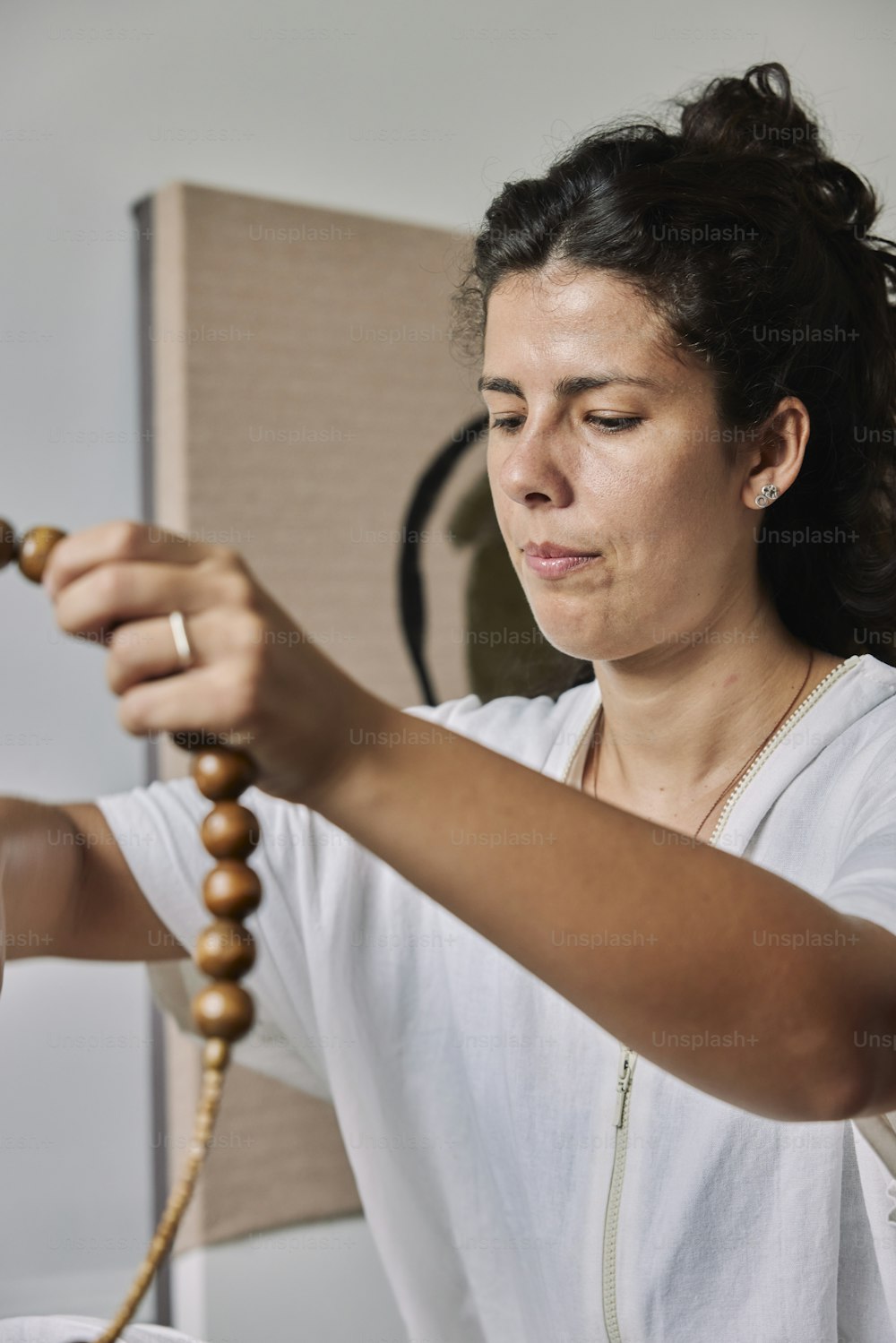 a woman in a white shirt is holding a wooden bead