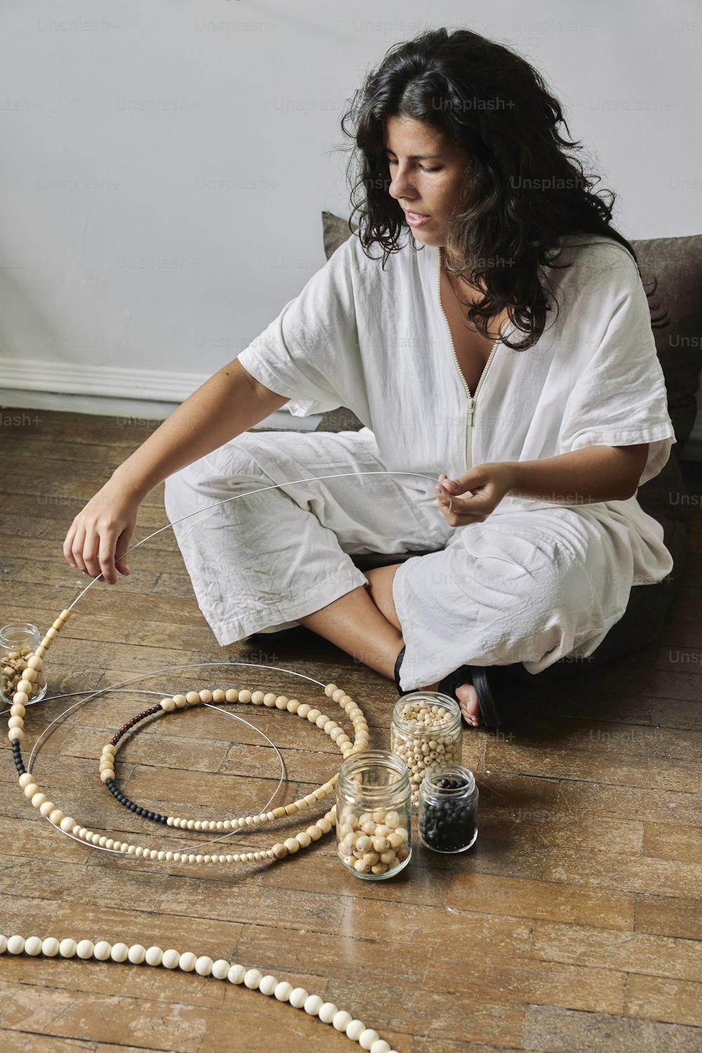 a woman sitting on the floor next to a jar of beads