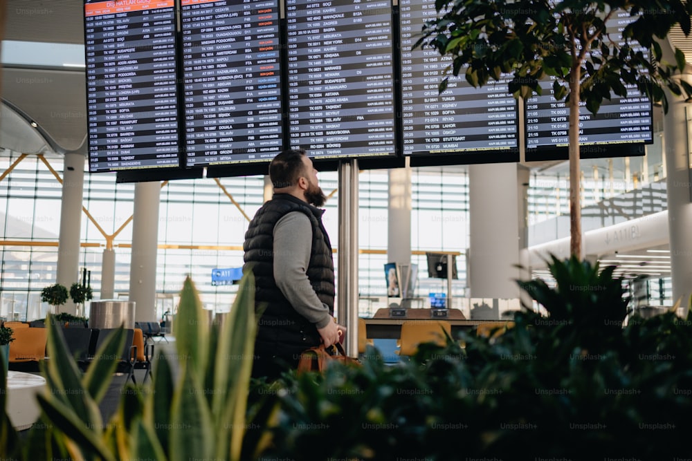Ein Mann steht vor einem großen Bildschirm in einem Flughafen