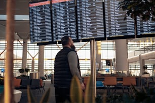 Un hombre parado frente a una gran pantalla en un aeropuerto