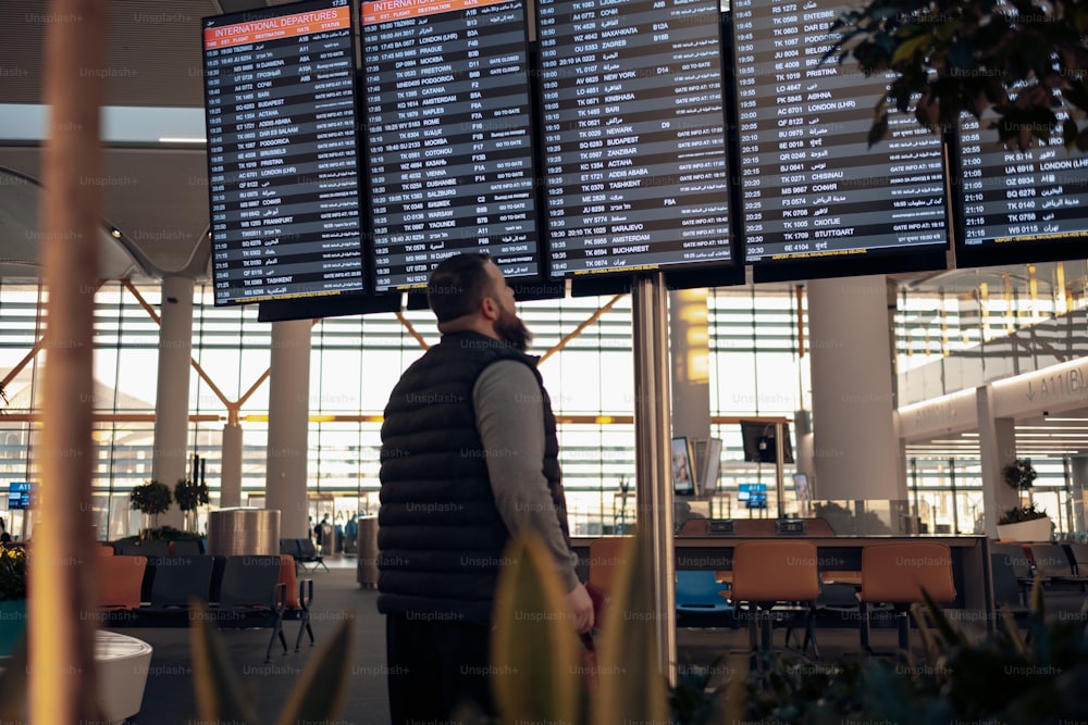Un hombre parado frente a una gran pantalla en un aeropuerto