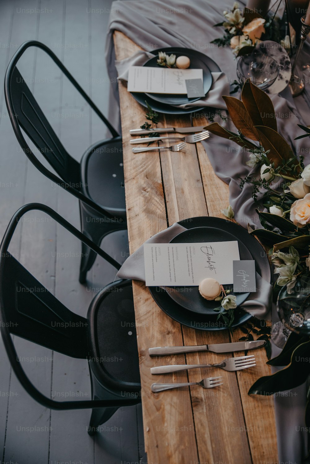 a wooden table topped with black plates and silverware