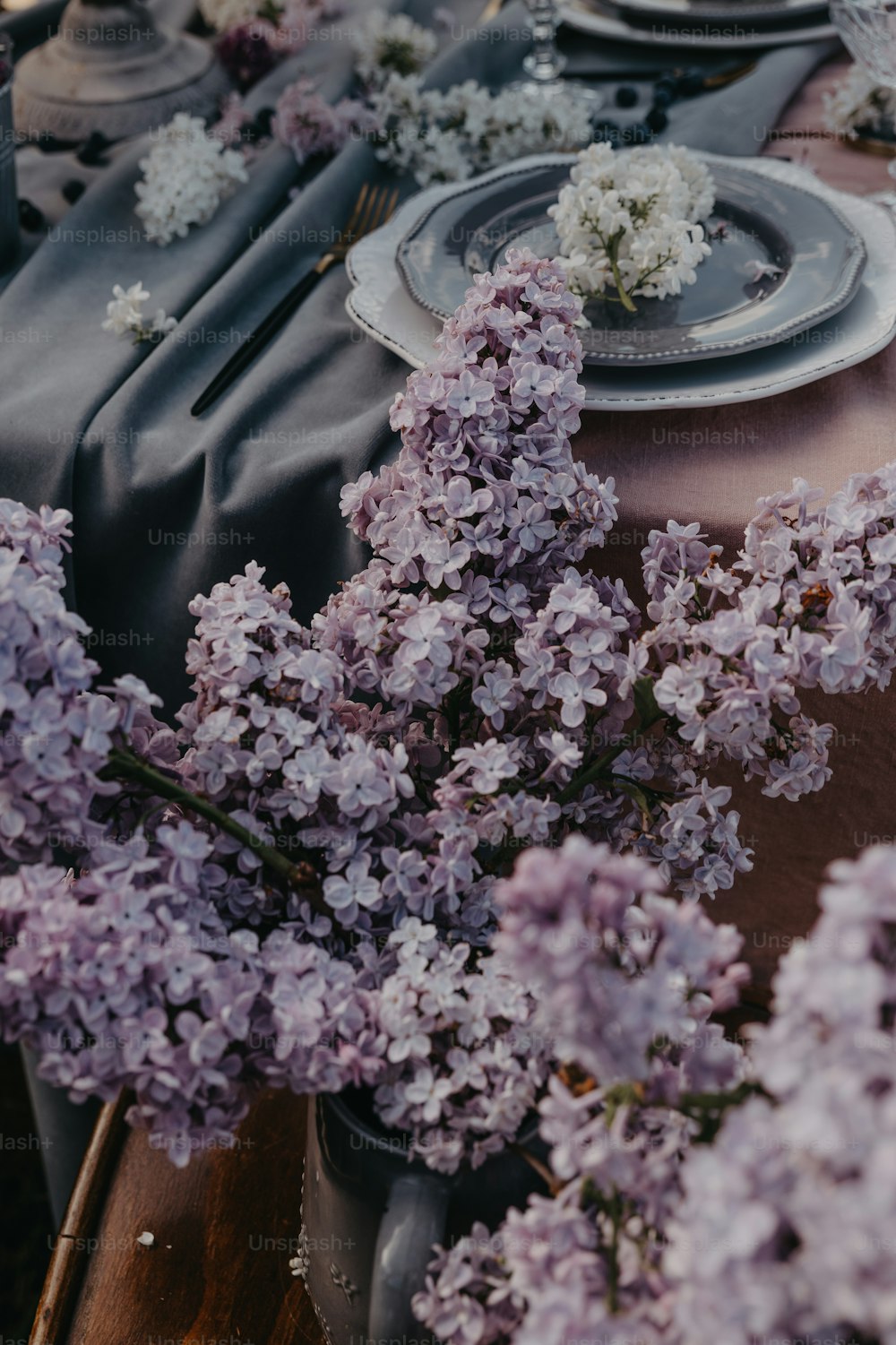 a table is set with purple flowers and plates