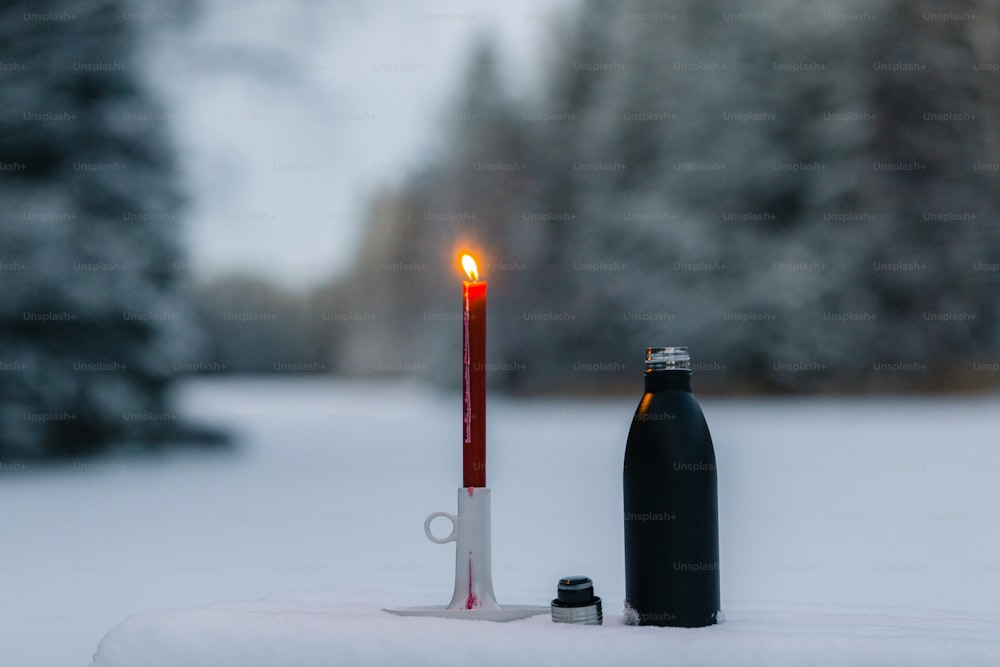 a candle and a bottle on a table in the snow