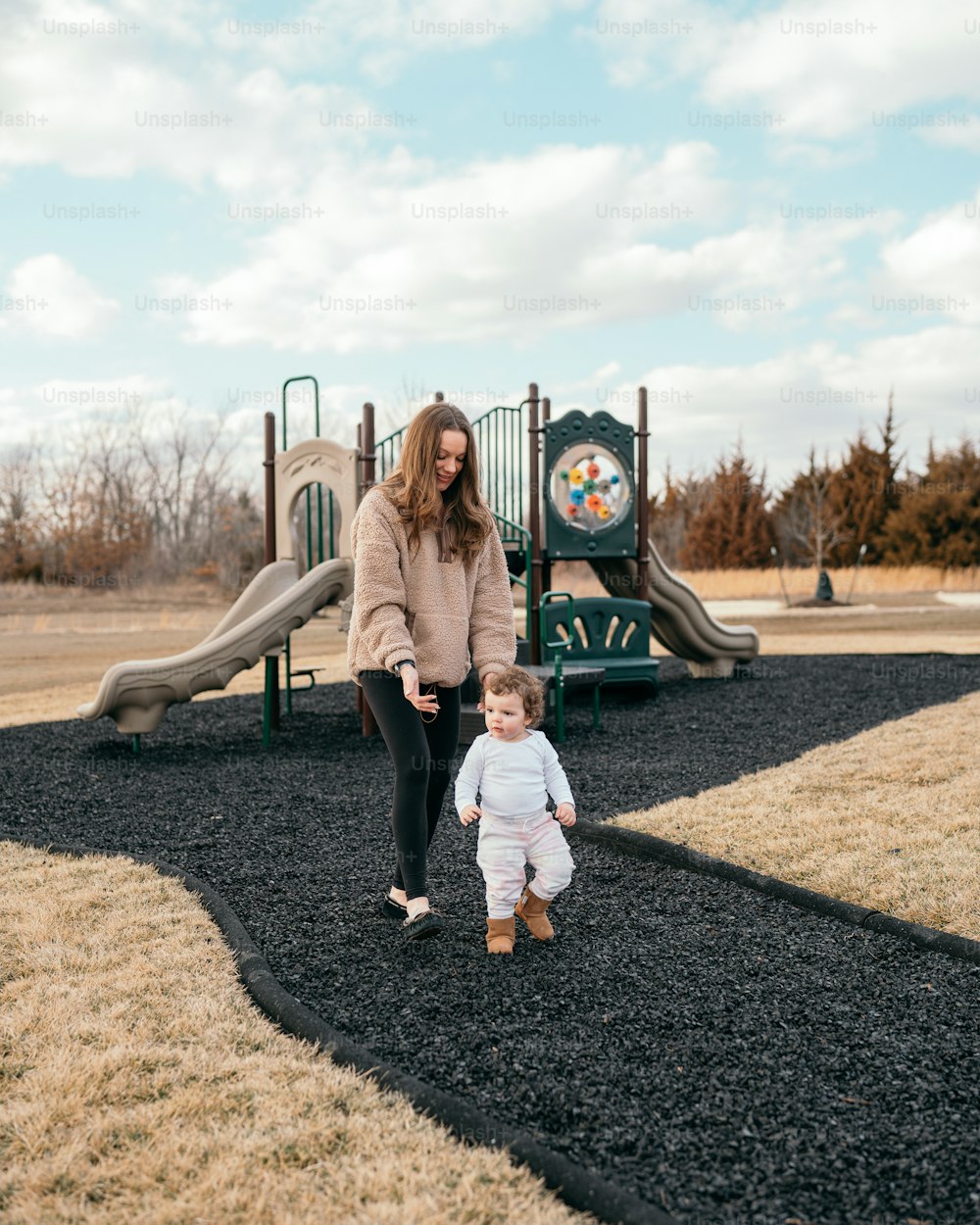 uma mulher e um bebê em pé na frente de um playground