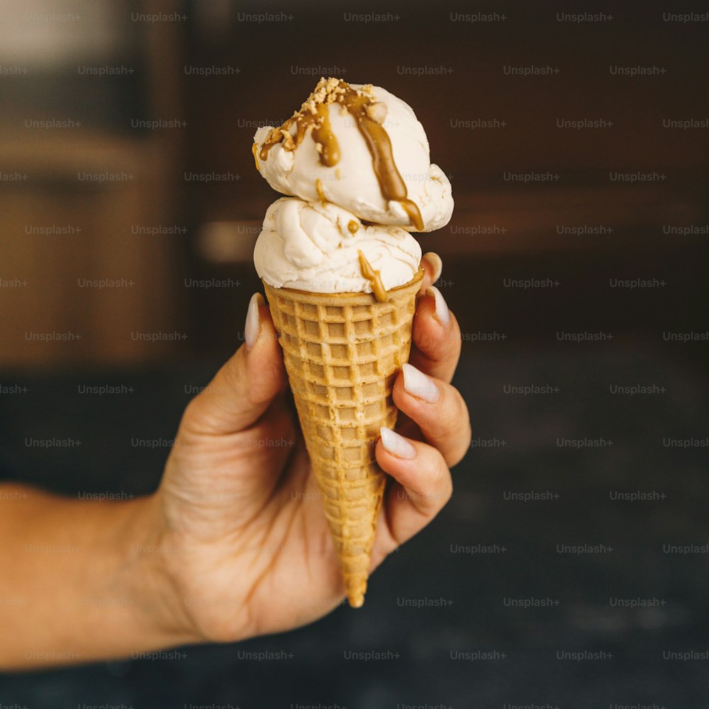 una mano sosteniendo un cono de helado con llovizna de caramelo