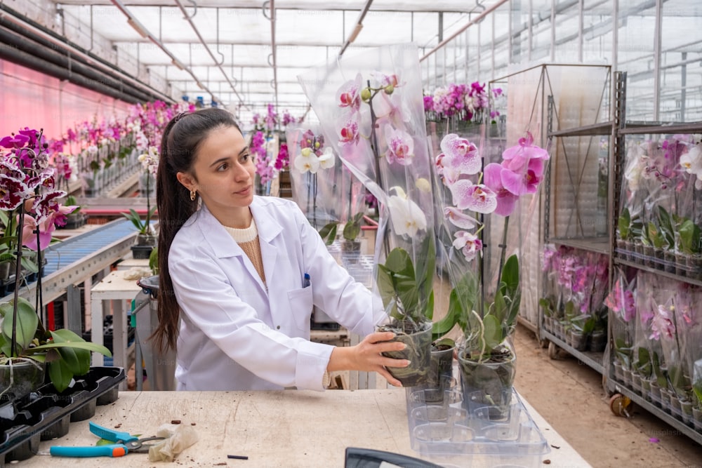 Una mujer con una bata blanca de laboratorio sosteniendo un jarrón de flores