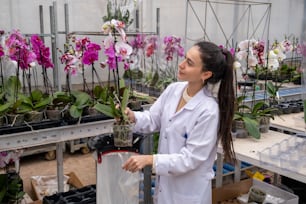 a woman in a white lab coat holding a plant in a greenhouse