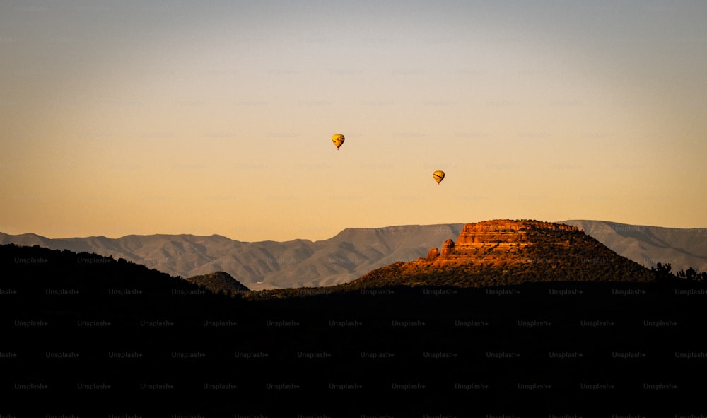 um par de balões de ar quente voando sobre uma montanha