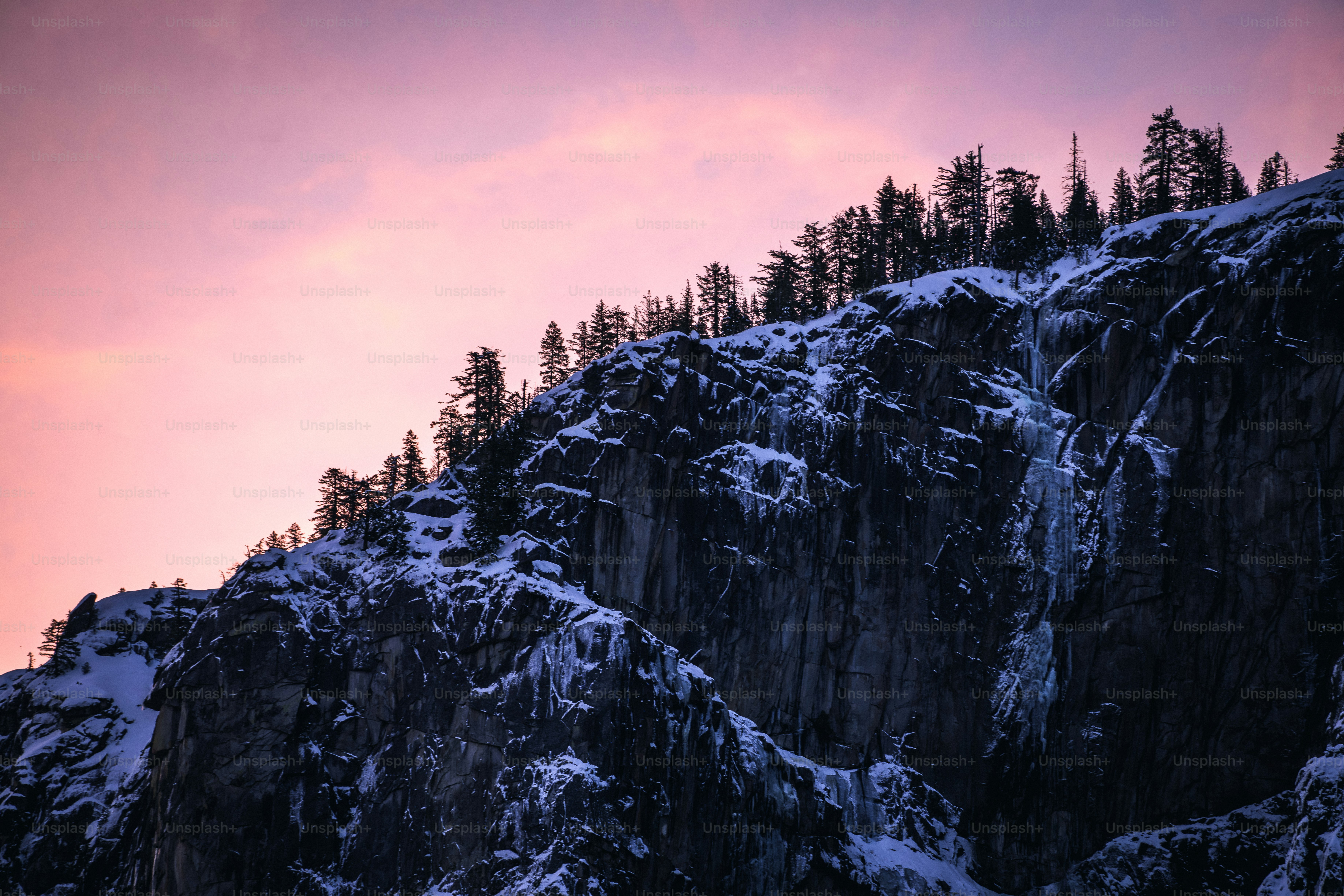 a very tall mountain covered in snow under a pink sky