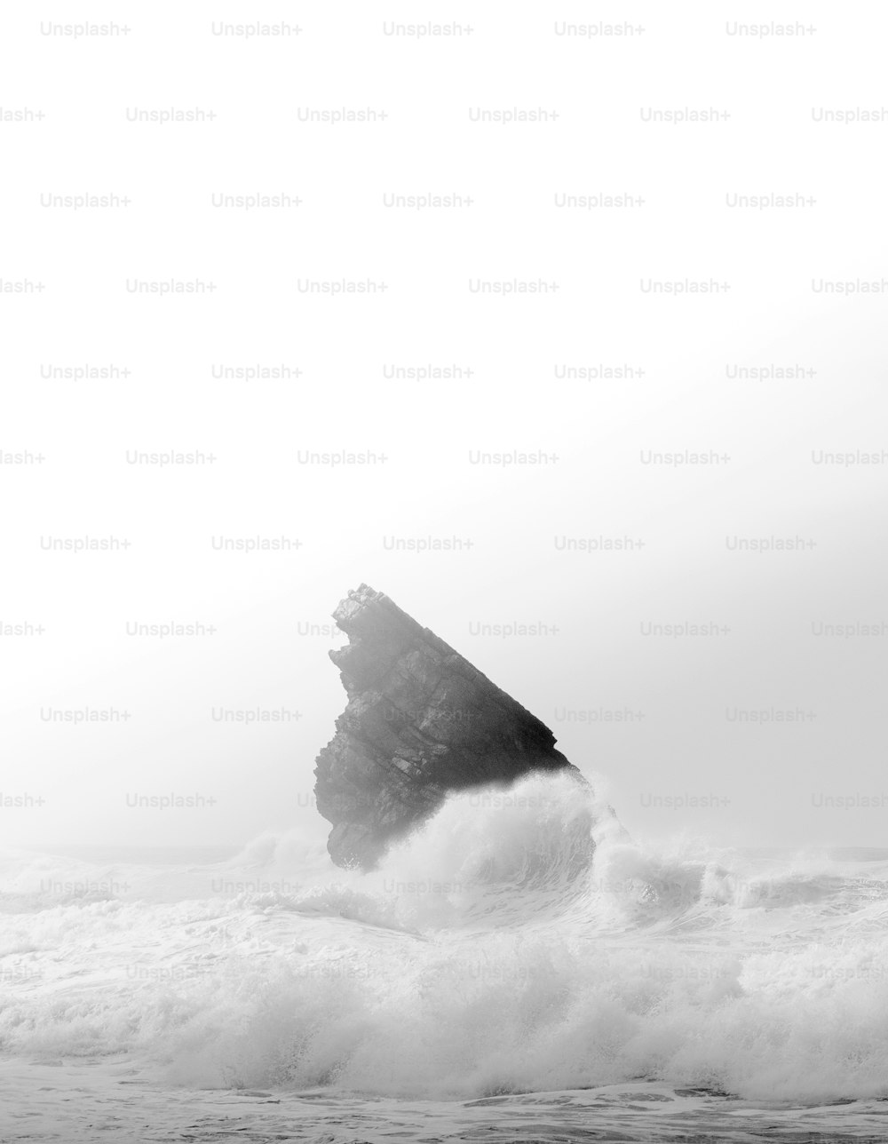 a black and white photo of a rock in the ocean