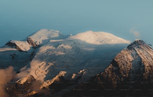 a mountain covered in snow and clouds under a blue sky