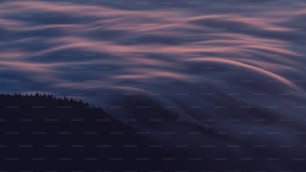 a mountain covered in clouds and trees under a purple sky