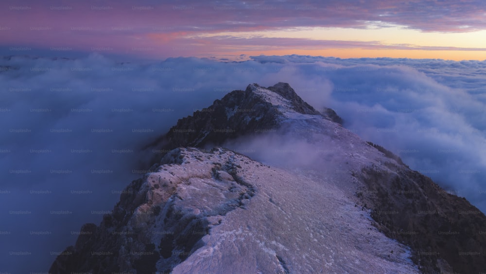 a mountain covered in snow and clouds under a pink sky